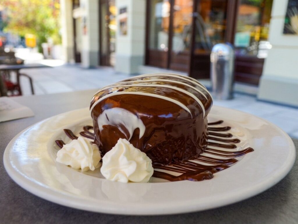 A chocolate-covered Tsoureki cake drizzled with white chocolate lines and served with whipped cream on a white plate at Terkenlis in Thessaloniki.
