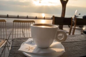 A cup of coffee on a wooden table at a seaside cafe along the Thessaloniki waterfront at sunset.