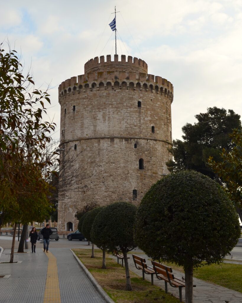Historic White Tower of Thessaloniki with a Greek flag and waterfront promenade