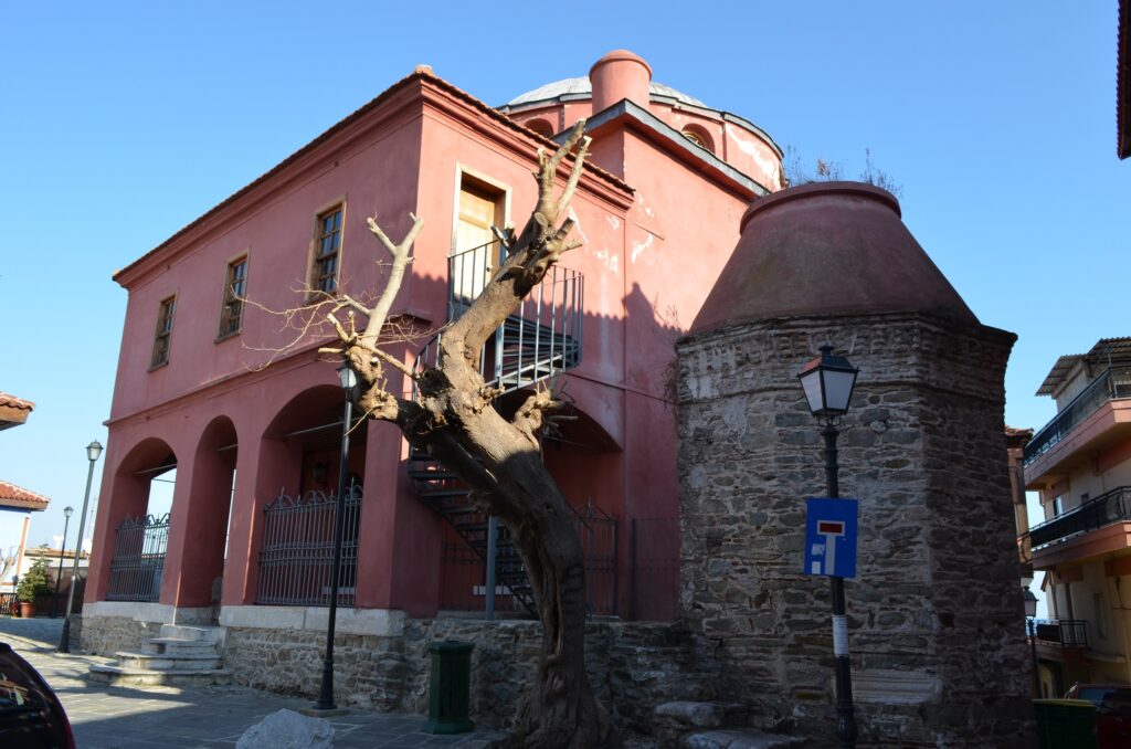 Halil Bey Mosque Kavala Greece Things to do in Kavala - Exterior view of the historic red-tinted Halil Bey Mosque with its truncated minaret, madrasa arches, and bare tree in Kavala's Old Town.