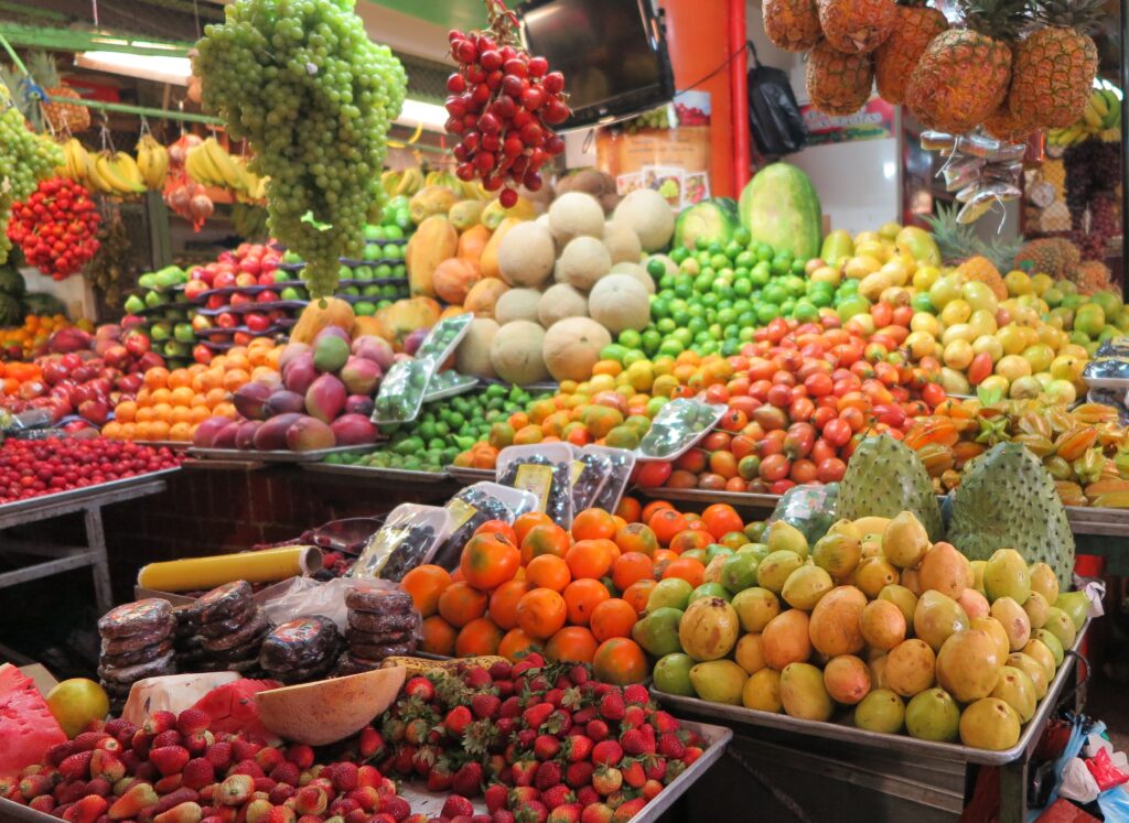 Vibrant stall filled with fresh Colombia tropical fruits including guanábana, granadilla, mangos, grapes, and pineapples in a local market.