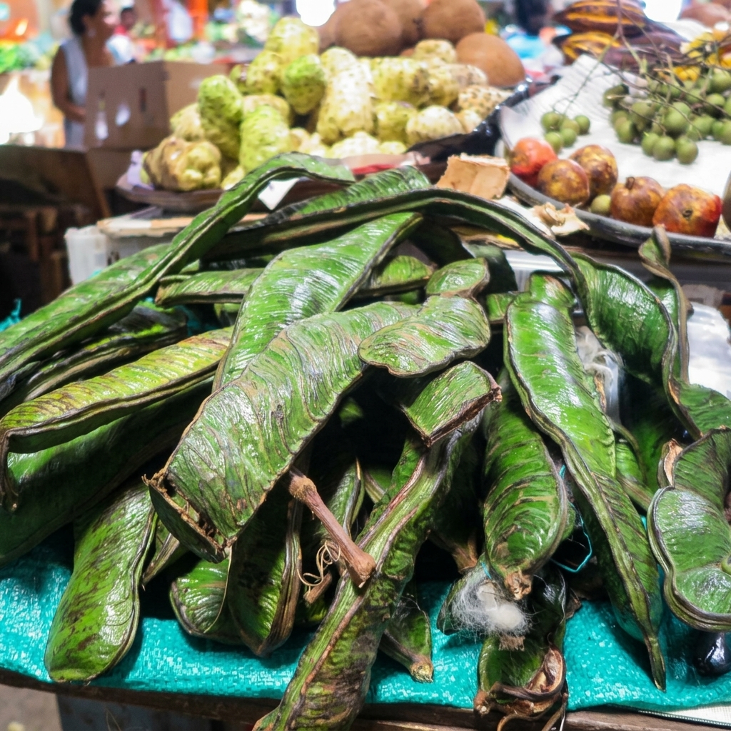 A close-up of large, dark green guama pods, also known as Ice Cream Beans, piled on a bright teal mesh surface at a busy market.
