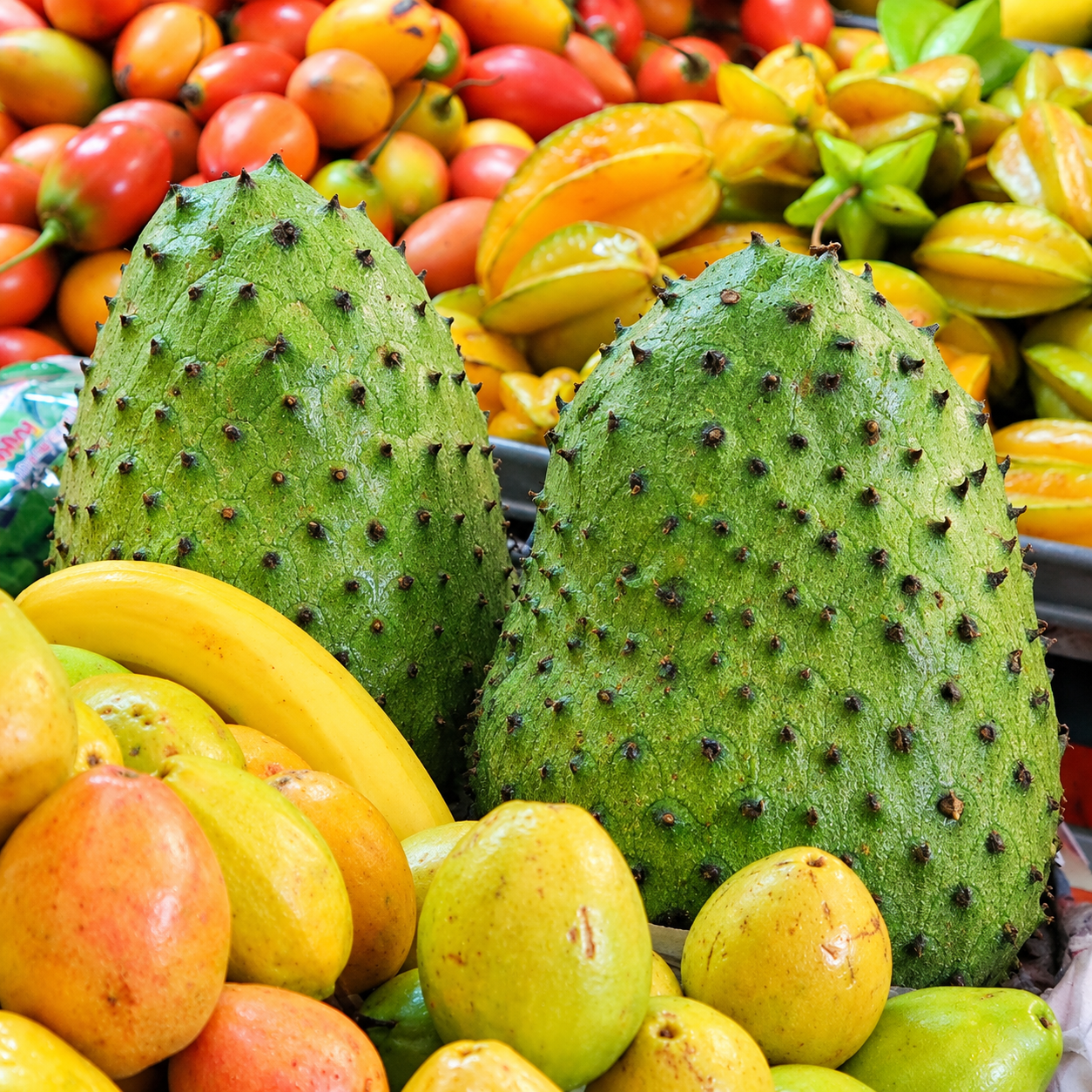 Two fresh Colombian guanabana (soursop) fruits displayed among colorful tropical fruits at a local market.
