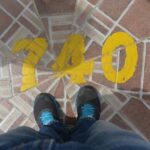 A visitor's shoes standing in front of the yellow-painted number “740” at the summit of El Peñón de Guatapé in Colombia.