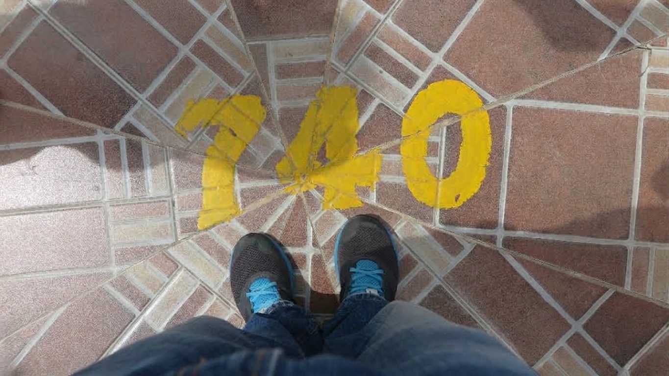 A visitor's shoes standing in front of the yellow-painted number “740” at the summit of El Peñón de Guatapé in Colombia.