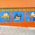 Colorful hand-painted baseboards, known as zócalos, featuring a pack donkey, a traditional bag and machete, and a farmer with a donkey on a bright orange wall in Guatapé, Colombia.