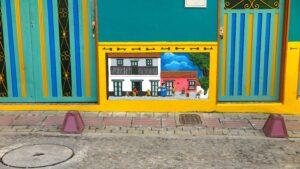 Vibrant teal and yellow building facade in Guatapé, Colombia, featuring a relief zócalo depicting a traditional street scene with colonial houses and playing children.