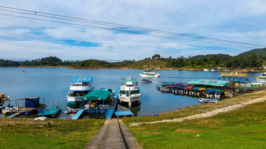Peñol Guatapé Reservoir A wide view of the Peñol Guatapé Reservoir in Colombia, with tour boats at a marina surrounded by lush green hills.